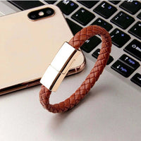 Charging cable bracelet in woven brown design resting on a phone next to laptop keyboard.