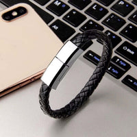 Charging cable bracelet stylishly woven with leather, resting next to a laptop, showcasing its dual functionality.